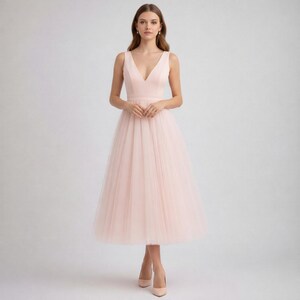 Op de afbeelding: Lichtroze mouwloze jurk met een V-hals en een tule rok. De jurk heeft een getailleerd lijfje en een midi-rok. Het model draagt bijpassende roze hakken. Geschikt voor speciale gelegenheden.
