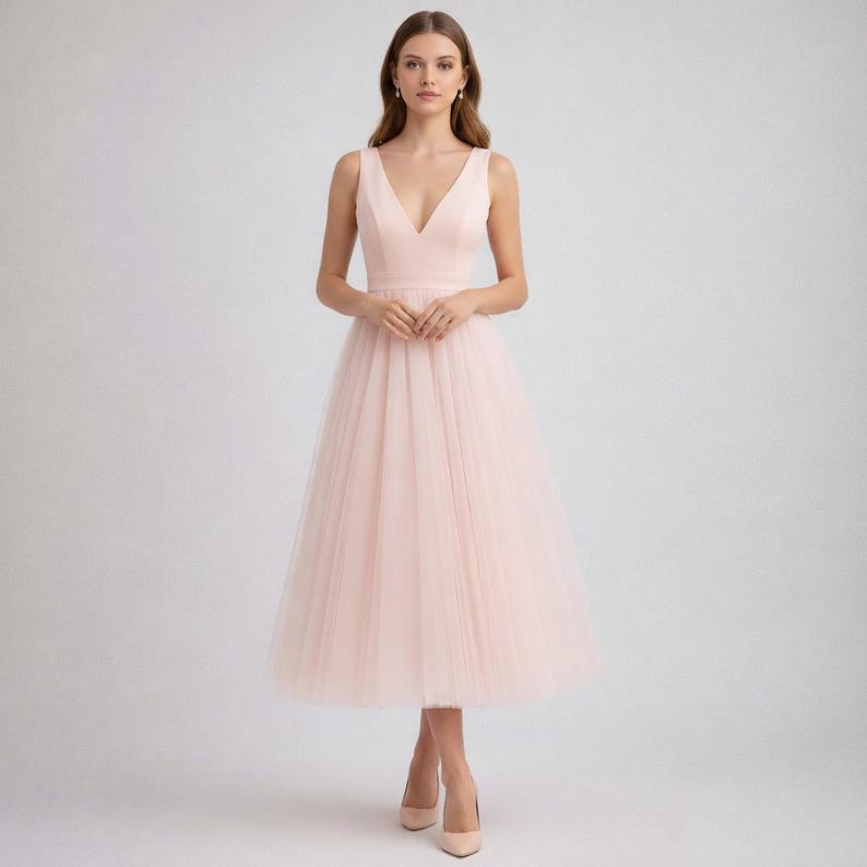 Op de afbeelding: Lichtroze mouwloze jurk met een V-hals en een tule rok. De jurk heeft een getailleerd lijfje en een midi-rok. Het model draagt bijpassende roze hakken. Geschikt voor speciale gelegenheden.