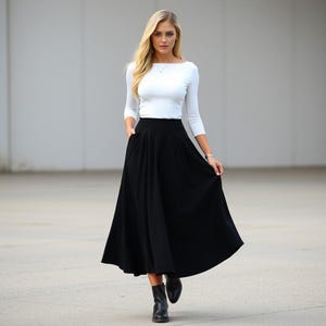 May include: A woman wearing a white long-sleeved shirt and a black midi skirt. The skirt has a high waist and a full, flowing silhouette.