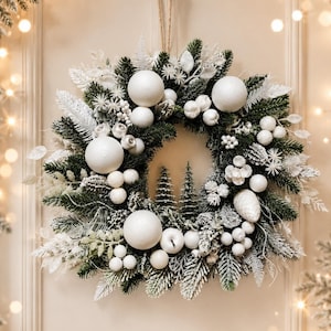 Peut inclure: Une couronne de fête circulaire composée de branches de pin vert foncé saupoudrées de neige artificielle blanche. La couronne est décorée de grandes sphères blanches mates, de grappes de petites baies blanches, de pommes de pin givrées et de sapins miniatures.