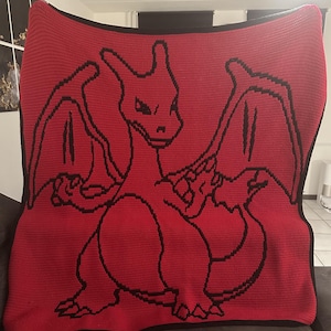 Könnte beinhalten: Rote Häkeldecke mit einer schwarzen Umrandung eines roten Drachen mit Flügeln. Der Drache steht mit ausgebreiteten Flügeln.