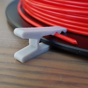 May include: A gray plastic filament guide for a spool of red filament. The guide is designed to hold the filament in place and prevent it from tangling.
