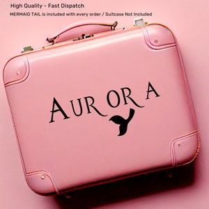 Peut inclure: Valise rose avec une queue de sir&egrave;ne noire et le nom "AURORA" &eacute;crit dessus.