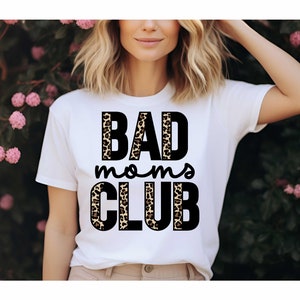 Pode incluir: Camiseta branca com o texto "BAD moms CLUB" em letras pretas com um design de estampa de leopardo atr&aacute;s das letras.