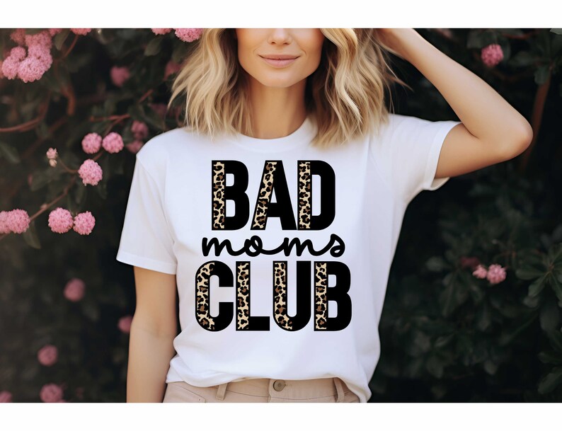 Pode incluir: Camiseta branca com o texto "BAD moms CLUB" em letras pretas com um design de estampa de leopardo atr&aacute;s das letras.