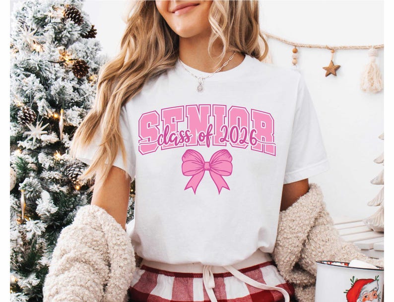 May include: White t-shirt with the text "SENIOR class of 2026" in pink block letters and a pink bow graphic. The shirt is a casual style, suitable for graduation celebrations.