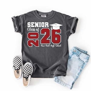 May include: Dark gray t-shirt with the text "SENIOR Class of 2026" in white and red. The shirt features a graduation cap graphic and the words "New York High School". The shirt is paired with light blue denim shorts and black and white checkered sneakers.