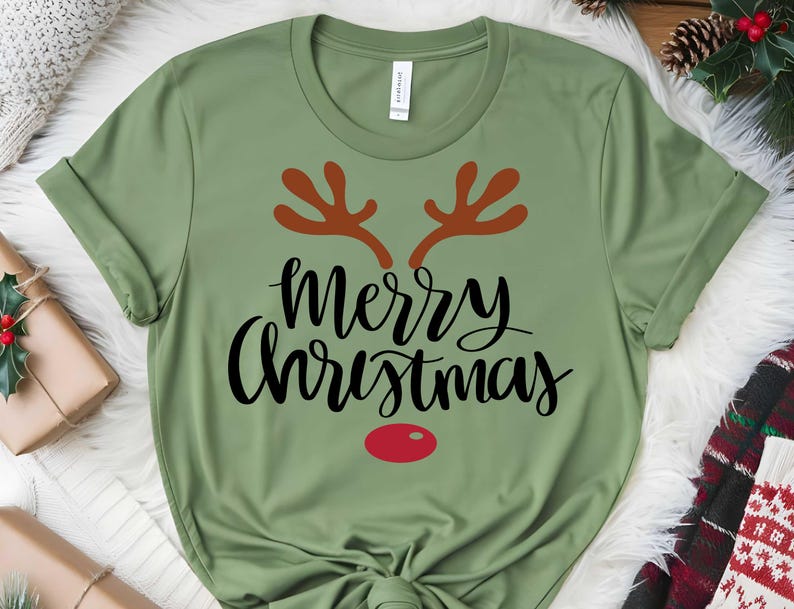 May include: A green t-shirt featuring the words "Merry Christmas" in black script, brown antlers, and a red nose. This festive t-shirt is a holiday apparel item.