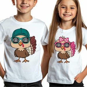 May include: Two white t-shirts with a cartoon turkey wearing sunglasses. The turkey on the left is wearing a blue baseball cap and the turkey on the right is wearing a pink bow. The text "Gobble Gobble" is on the sunglasses of both turkeys.