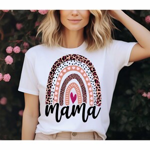 Pode incluir: Camiseta branca com um design de arco-&iacute;ris com estampa de leopardo rosa, marrom e preto, bolinhas brancas e cora&ccedil;&otilde;es rosas. O arco-&iacute;ris tem um cora&ccedil;&atilde;o rosa no centro e a palavra "mama" est&aacute; escrita abaixo.
