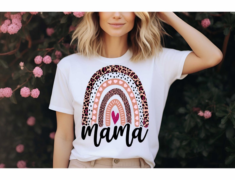 Pode incluir: Camiseta branca com um design de arco-&iacute;ris com estampa de leopardo rosa, marrom e preto, bolinhas brancas e cora&ccedil;&otilde;es rosas. O arco-&iacute;ris tem um cora&ccedil;&atilde;o rosa no centro e a palavra "mama" est&aacute; escrita abaixo.