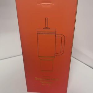 May include: A rectangular coral-colored product box featuring a black line drawing of a tumbler with a handle, lid, and straw. The text on the box reads Quencher H2.0 Tumbler 40 oz | 1.18 L. The packaging is tall and vertical with a flat top.