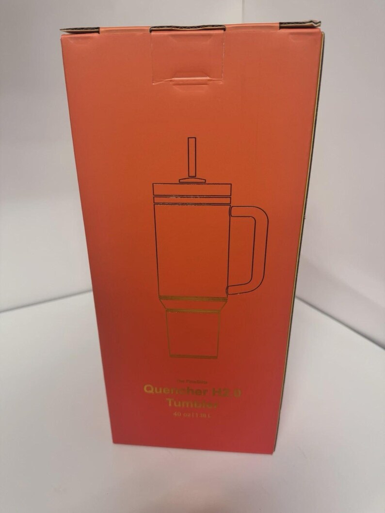 May include: A rectangular coral-colored product box featuring a black line drawing of a tumbler with a handle, lid, and straw. The text on the box reads Quencher H2.0 Tumbler 40 oz | 1.18 L. The packaging is tall and vertical with a flat top.