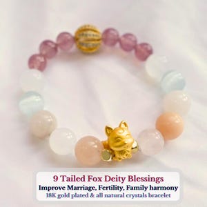 Könnte beinhalten: Ein Armband aus rosa, weißen und hellblauen Perlen mit einem goldenen 9-schwänzigen Fuchs-Anhänger. Das Armband ist 18 Karat vergoldet und besteht aus natürlichen Kristallen. Der Text "9 Tailed Fox Deity Blessings Improve Marriage, Fertility, Family harmony 18K gold plated & all natural crystals bracelet" steht unter dem Armband.