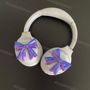 May include: White wireless headphones with a blue and purple iridescent bow on each earcup.