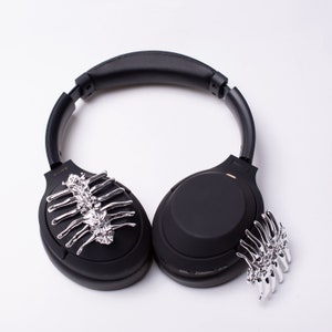 May include: Black wireless headphones with silver skeleton-shaped embellishments on each earcup.