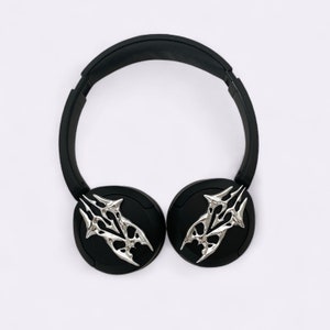 Puede incluir: Auriculares negros con detalles plateados en forma de calavera en las almohadillas.