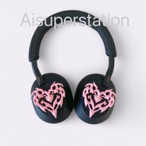 May include: Black over-ear headphones with pink heart-shaped designs on the earcups. The headphones have the word "SONY" written on the side.