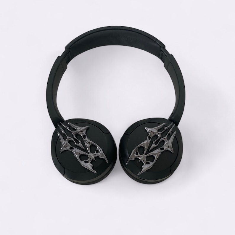 Puede incluir: Auriculares inal&aacute;mbricos negros con un dise&ntilde;o plateado intrincado en cada auricular.