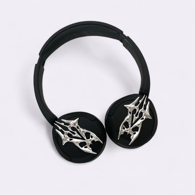 Puede incluir: Auriculares negros con dise&ntilde;os plateados estilizados de tipo tribal en las almohadillas.