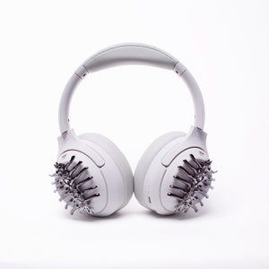 May include: White wireless headphones with a silver, spiky design on each earcup.
