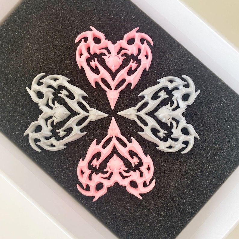 May include: Four heart-shaped charms, two are pink and two are gray. Each charm has a detailed, intricate design with a pointed tip at the bottom.