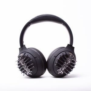 May include: Black wireless headphones with a unique design featuring a silver and black decorative element on each earcup.