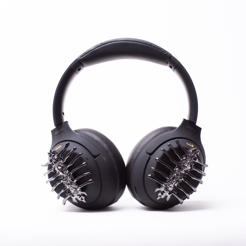 May include: Black wireless headphones with a unique design featuring a silver and black decorative element on each earcup.