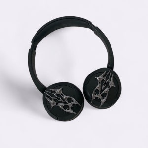 Puede incluir: Auriculares negros con un dise&ntilde;o tribal plateado en cada auricular. Los auriculares tienen una diadema negra.