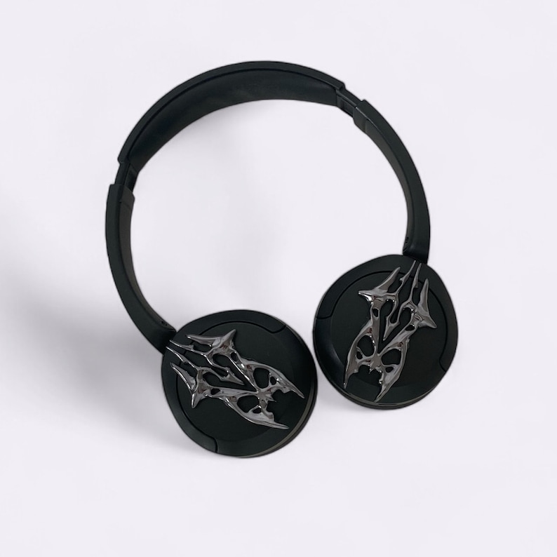 Puede incluir: Auriculares negros con un dise&ntilde;o tribal plateado en cada auricular. Los auriculares tienen una diadema negra.