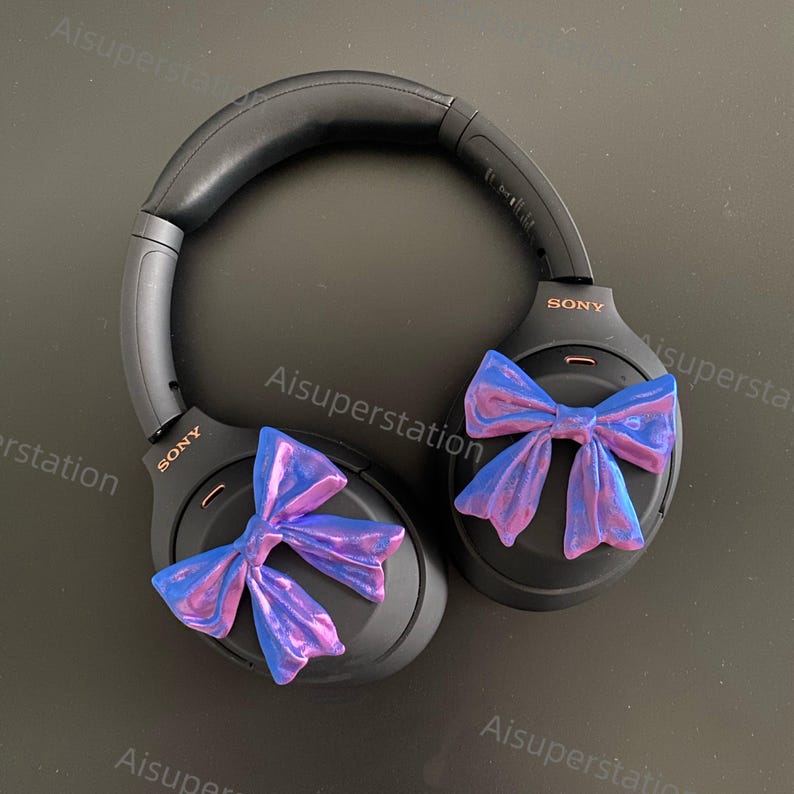 May include: Black over-ear headphones with a pink and blue bow on each earcup. The headphones have the word "SONY" printed on each earcup.