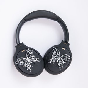 May include: Black over-ear headphones with silver butterfly-shaped embellishments on each earcup. The headphones have the word "SONY" printed on each earcup.