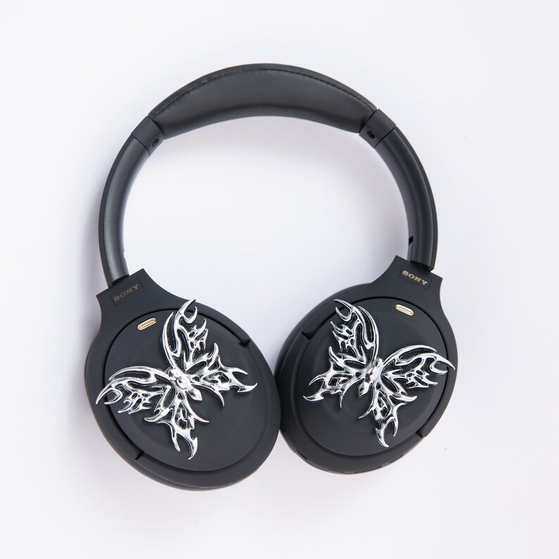 May include: Black over-ear headphones with silver butterfly-shaped embellishments on each earcup. The headphones have the word "SONY" printed on each earcup.