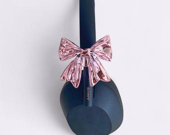 May include: Black Sony headphones with a shiny pink bow attached. The headphones have a sleek, modern design and the bow adds a touch of elegance. The Sony logo is visible on the headphones.