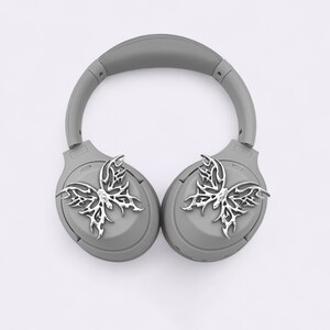 May include: Gray wireless headphones with silver butterfly-shaped embellishments on each earcup.