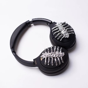 May include: Black over-ear headphones with silver decorative accents on each earcup. The accents resemble a skeletal structure.