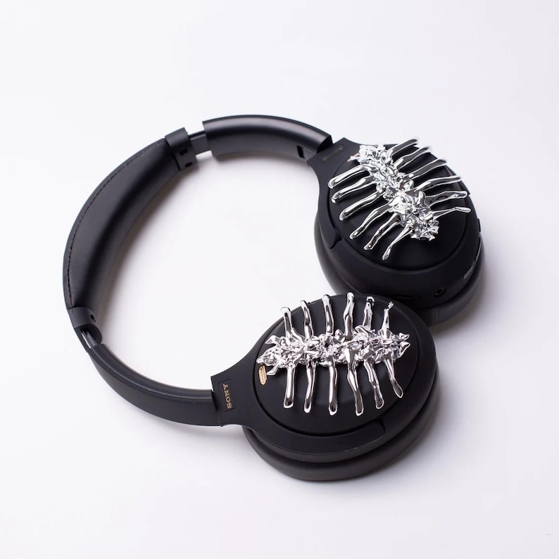 May include: Black over-ear headphones with silver decorative accents on each earcup. The accents resemble a skeletal structure.