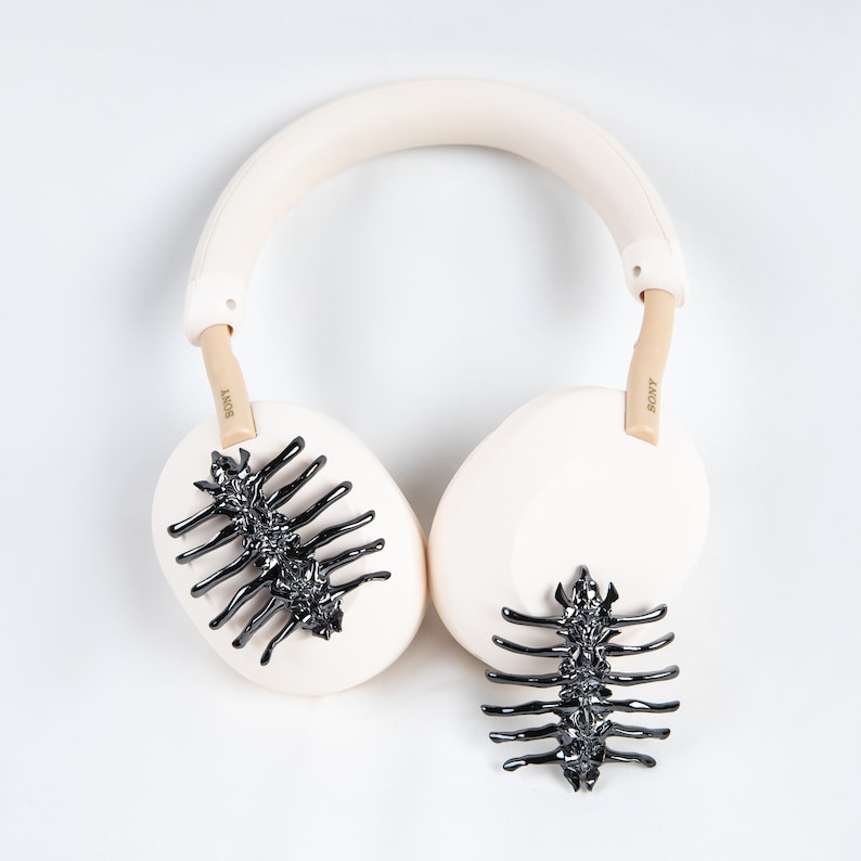 May include: Cream-colored Sony headphones with black, spine-like embellishments on the earcups. The headband and earcups are a soft cream color, with tan-colored arms. The Sony logo is visible on the arms.
