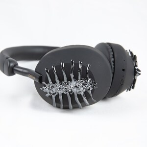 May include: Black over-ear headphones with a silver, spiky, abstract design on one earcup. The headphones have the word "SONY" printed on the side.