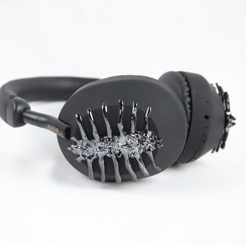 May include: Black over-ear headphones with a silver, spiky, abstract design on one earcup. The headphones have the word "SONY" printed on the side.