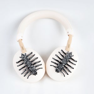May include: Cream-colored Sony headphones with black, stylized insect-like designs on the earcups. The headband and earcups are a soft cream color, with the Sony logo visible on the arms. The design is a unique, artistic take on headphones.