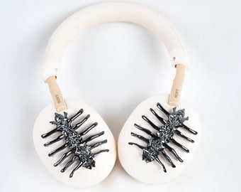 May include: Cream-colored Sony headphones with black, stylized insect-like designs on the earcups. The headband and earcups are a soft cream color, with the Sony logo visible on the arms. The design is a unique, artistic take on headphones.