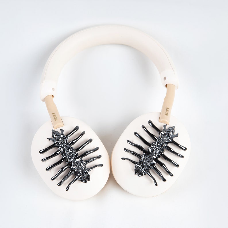 May include: Cream-colored Sony headphones with black, stylized insect-like designs on the earcups. The headband and earcups are a soft cream color, with the Sony logo visible on the arms. The design is a unique, artistic take on headphones.
