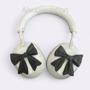 K&ouml;nnte beinhalten: Wei&szlig;e Over-Ear-Kopfh&ouml;rer mit schwarzen Schleifen an jedem Ohrpolster. Die Kopfh&ouml;rer haben den Schriftzug "SONY" auf der Seite jedes Ohrpolsters.