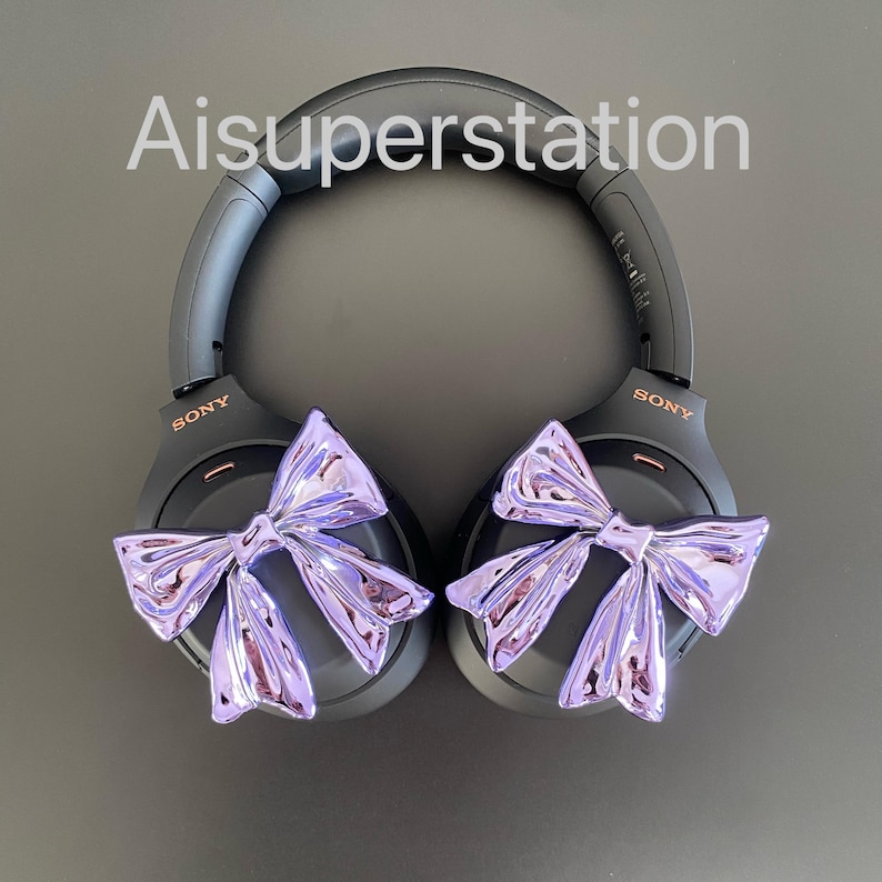 Pu&ograve; includere: Un paio di cuffie over-ear nere con fiocchi viola attaccati ai padiglioni auricolari. Le cuffie hanno la scritta "SONY" stampata su ogni padiglione.