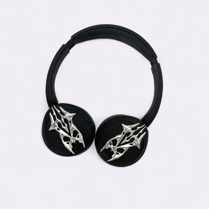 Puede incluir: Auriculares negros con un dise&ntilde;o de calavera plateada en cada auricular.