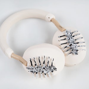May include: Cream-colored headphones with silver-colored spine-like embellishments on the earcups. The headband and earcups are a soft cream color, with the brand name "SONY" printed on the arms.