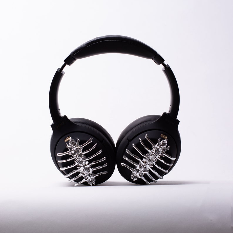 May include: Black wireless headphones with a silver skeletal design on the earcups.