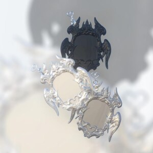 May include: Two decorative mirrors. One is silver with an ornate, angel-wing design. The other is black with a similar design. Both mirrors have a heart-shaped accent at the top.