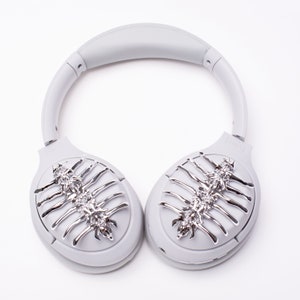 May include: Gray over-ear headphones with silver decorative accents on the earcups. The accents are in the shape of a stylized skeletal design.
